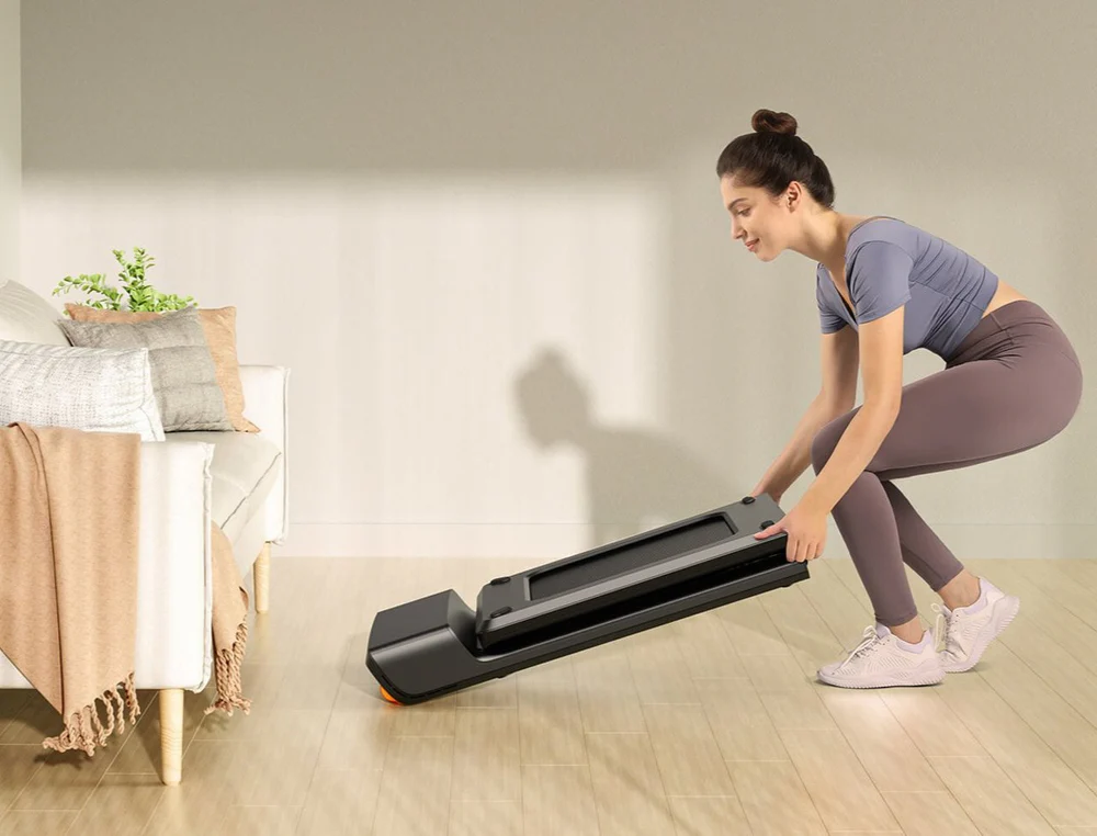 WalkingPad KingSmith A1 Pro doblada a la mitad y guardada debajo de un mueble en una sala moderna.